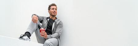 Healthy sport man drinking red smoothie breakfast juice banner panoramic crop relaxing sitting at home in casual activewear sitting on outdoor gym health club, white background.の写真素材
