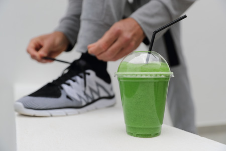 Green smoothie man tying running shoes laces ready to run in urban city. Healthy active lifestyle,...