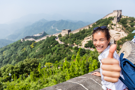 Happy tourist girl at Great Wall of china doing thumbs up hand sign having fun at famous Badaling ruins during travel holidays at Chinese destination. Asia vacation.の写真素材