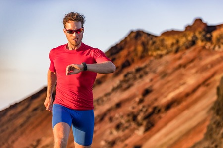 Athlete runner checking cardio on sports smartwatch jogging on outdoor run track. Running man...