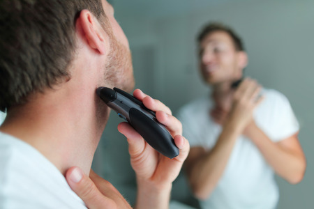 Man shaving beard using electric trimmer shaver. Male beauty grooming concept. Home lifestyle young...