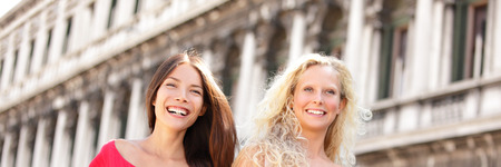 Beautiful multiethnic models women walking outdoor on street. Perfect smile laughing healthy Asian and Caucasian girls, blonde and brunette, happy multiracial people on summer travel Europe vacation.の写真素材