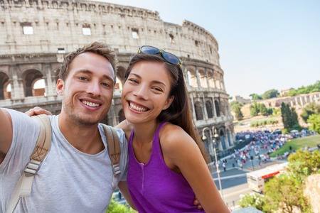 Travel selfie couple taking photo with phone at colosseum famous landmark in Rome city. Europe Italy summer vacation young people smiling. Backpacking road trip.の写真素材