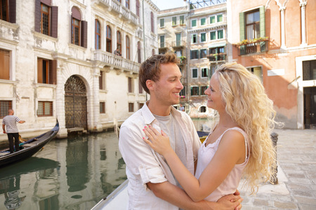 Romantic honeymoon couple in Venice city street near Grand Canal in love hugging in summer Italy travel. Blonde woman and man looking at each other on Europe vacation holidays. .の写真素材