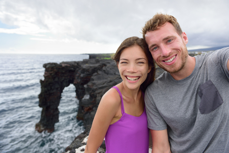 Selfie couple on nature travel Hawaii vacation. Young people taking phone picture at the Holei Sea Arch, tourist attraction on Big Island at the Volcanoes National park.の写真素材