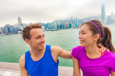 Happy couple runners living a fit active healthy lifestyle in Hong Kong city laughing together after run workout outdoors. Interracial people happy wearing sportswear on sightseeing tourism travel.の写真素材