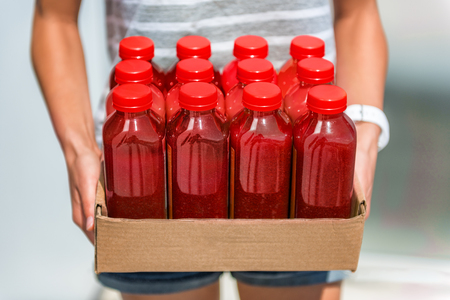 Beet juice red smoothie juicing bottles box of cold pressed vegetable juices. Woman holding delivery box. Health trend for cleansing of organic raw juices. Juicing for diet cleansing detox.の写真素材