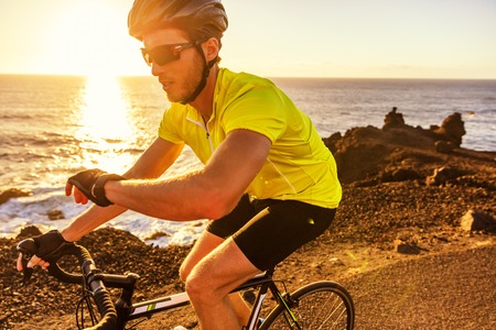 Cyclist biking looking at smartwatch while riding road bike. Athlete biker using activity tracker gps fitness watch on biking workout in sunset. Sports man using his watch app for fitness tracking.の写真素材