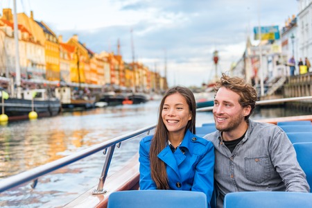 Copenhagen tourists people on Denmark travel holiday cruise boat tour in old port. Young multiracial couple travelers relaxing enjoying view of Nyhavn danish destination in Europe, fall or spring.の写真素材
