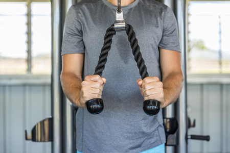 Fitness man exercising triceps muscles in the gym with pull-down ropes fitness equipment machine attachement. Arms strength training at health club.の写真素材