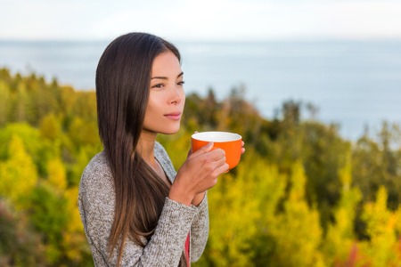 Nature outdoors coffee drinking woman relaxing in forest autumn sunshine enjoying her morning coffee. Happy multiracial canadian Asian Chinese / Caucasian girl in her 20s, Canada.の写真素材