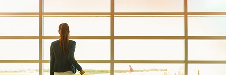 Airport travel businesswoman on business trip vacation waiting for flight looking out the window at tarmac. Banner panoramic header with copy space on windows background. People traveling lifestyle.の写真素材