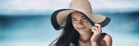 Beach sun tan skin care Asian beauty woman happy on beach vacation panoramic banner wearing sunhat. Healthy suntan skincare concept with hat.の写真素材