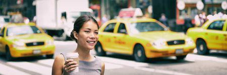 New York city commute - Asian business woman walking to work in the morning commuting drinking coffee cup on NYC street with yellow cabs in the background banner. People commuters lifestyle.の写真素材
