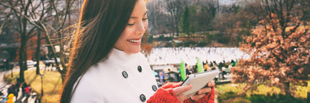 Woman walking happy in Central park, New York City in winter with Wollman skating rink using tech...