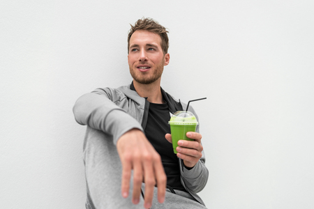 Healthy man drinking green smoothie spinach juice at home relaxing. Young adult eating detox diet, active lifestyle.の写真素材