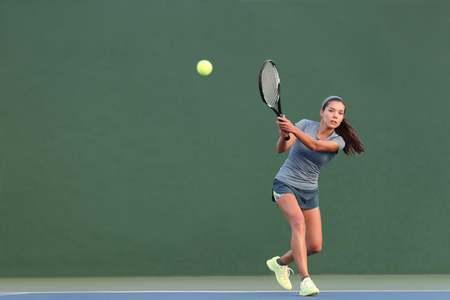 Tennis playing woman hitting ball on green hard court. Asian athlete girl returning serve with racket wearing skort and shoes.の写真素材
