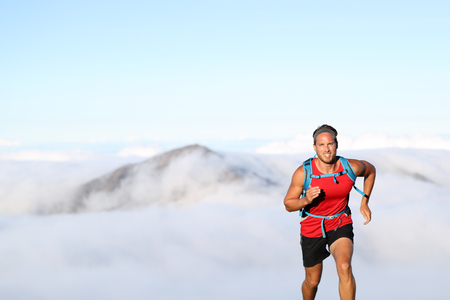 Trail runner man athlete running in mountains outdoor nature with mountain peak in clouds in background.の写真素材