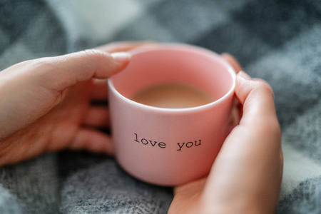 Winter warm coffee cup woman relaxing at home cozy with wool blanket - morning breakfast girl drinking with the words LOVE YOU written on pink mug for valentines day. Romantic quote.の写真素材