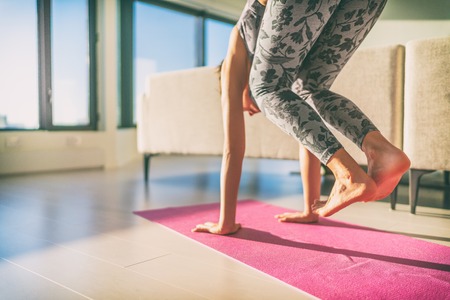 Yoga practicing to handstand - beginner girl doing jump through on hands on exercise mat at home....