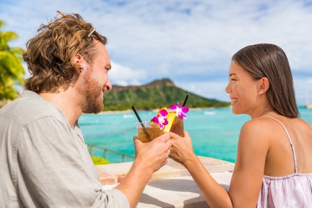 Couple toasting drinks flirting on date at beach bar in Waikiki, Honolulu,Hawaii. Young people going out drinking mai tai drink alcoholic cocktails.の写真素材