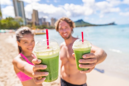 Fitness couple drinking green smoothie at beach. Man and woman holding vegetable smoothies after running sport fitness training. Healthy clean eating lifestyle concept.の写真素材
