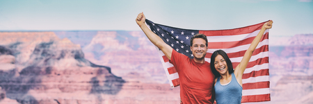 USA flag american travel tourists people holding flag in Grand Canyon banner background. Happy young interracial couple cheering during summer holidays.の写真素材