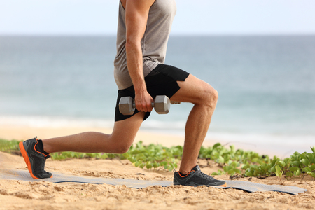 Lunge leg workout with dumbbells weights. Fitness man doing lunges training legs on beach summer outdoors with weight.の写真素材