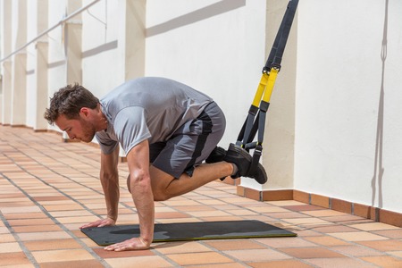 Gym man suspension straps training abs core body muscles on fitness equipment. Stomach abdominals workout healthy lifestyle sport. Floor exercise doing crunches with legs.の写真素材