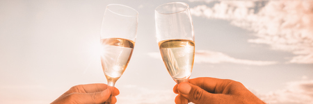 Couple toasting wine glasses for celebration. Champagne toast in luxury restaurant. Two people holding flutes doing cheers. Banner panorama crop on sunset background.の写真素材