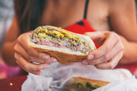 Cuban sandwich closeup woman holding local food at typical cafe outside. Pressed cuban bread with roasted pork, salami sausage, swiss cheese, mustard, typical cuba dish.の写真素材