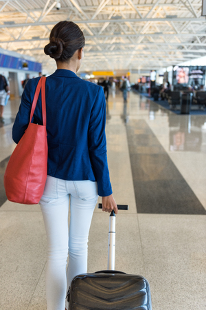 Woman traveler walking through airport terminal going to gate carrying purse and carry-on hand luggage for flight travel.の写真素材