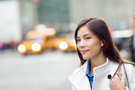 New Yorker woman walking on New York City street waiting for car lift rideshare taxi. Asian young professional with yellow taxi cabs cars traffic in background. Biracial person.の写真素材