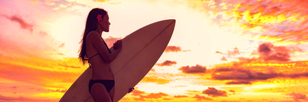 Surfer bikini girl on Hawaii beach holding surf board watching ocean waves at sunset. Silhouette of...