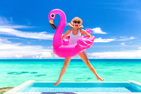 Summer vacation fun funny woman jumping with flamingo swimming pool float around waist excited of tropical hotel holiday.の写真素材