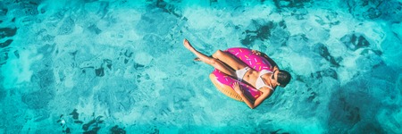 Beach vacation woman relaxing in pool float donut inflatable ring floating on turquoise ocean water...
