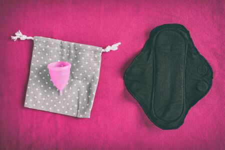 Reusable eco-friendly feminine hygiene period products - menstrual cup and black organic cotton menstruation pad - cloth menstrual pads to wash. Top view on red towel background.の写真素材