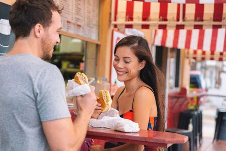 Happy couple eating sandwiches in typical retro cafe in Florida. Cuba sandwich local food. Summer travel tourist lifestyle young Asian woman smiling eating lunch outside.の写真素材