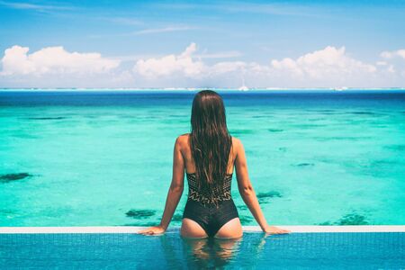 Sexy swimsuit model at luxury infinity pool overwater bungalow hotel showing off cheeky black lace...