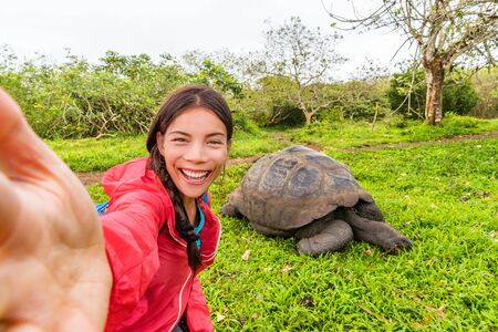 Adventure travel tourist on Galapagos Islands taking selfie phot by Giant Tortoises on Santa Cruz Island in Galapagos Islands. Animals and nature in Galapagos highlands.の写真素材