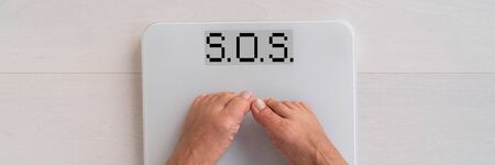 SOS written on weight scale screen woman weighting herself in on bathroom floor needing help to lose fat - obesity banner panoramic concept.の写真素材