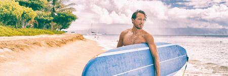 Surfer man relaxing on beach carrying his long board after surf session on Hawaii ocean waves....