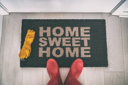 Rain boots selfie walking on doormat entrance welcome sign saying Home Sweet Home with yellow umbrella for autumn real estate moving in concept.の写真素材