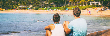 Happy couple on beach vacation travel holiday in Hawaii. Asian girl laughing on back of boyfriend piggybacking girlfriend in Lanikai, Oahu island, Hawaii USA destination.の写真素材