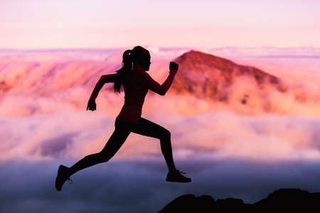 Trail runner nature landscape running woman silhouette on mountains background in cold weather with pink clouds at sunset. Amazing scenic view of peaks in altitude.の写真素材