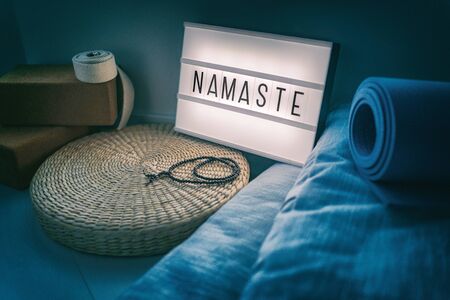 Yoga studio class sign lightbox with letters writing NAMASTE glowing in the night light with natural accessories, rubber mat, cork blocks, organic cotton strap and pillows, straw meditation pillow.の写真素材