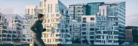 City lifestyle winter run runner athlete man jogging outside on modern apartment building background panoramic banner. Running active living people panorama.の写真素材