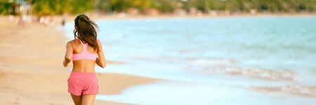 Runner running on sunset beach ocean landscape banner panoramic background. Sport health and fitness woman athlete jogging outdoors Fit girl wearing pink sports bra and summer shorts.の写真素材
