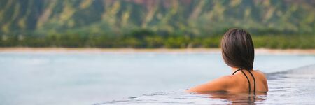 Luxury vacation woman travel tourist relaxing in infinity swimming pool on summer travel at tropical beach resort. girl alone on wellness spa relaxation outside in nature landscape banner panorama.の写真素材