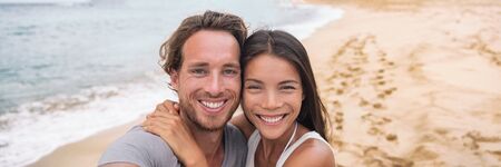 Tourists on beach Smiling beautiful young multiracial couple taking selfie on vacation panoramic...